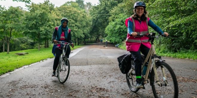 Two women cycling in pink vests in a park.